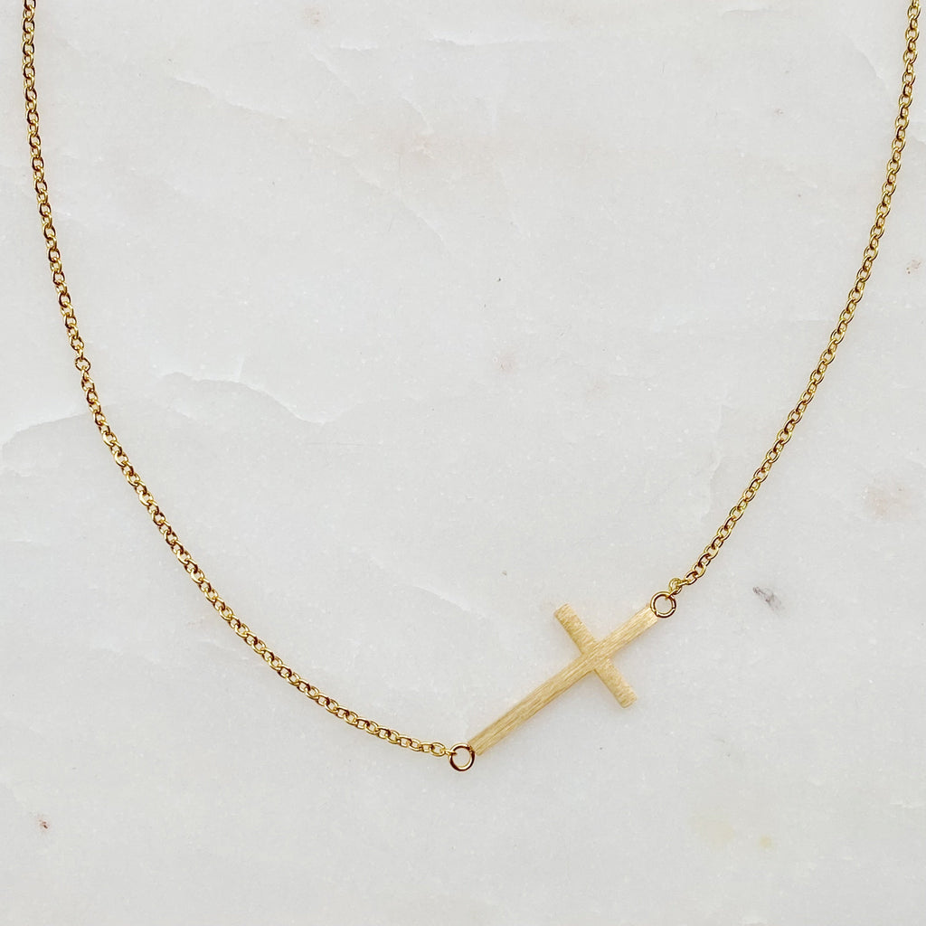 Gold necklace with a small cross pendant on a light background