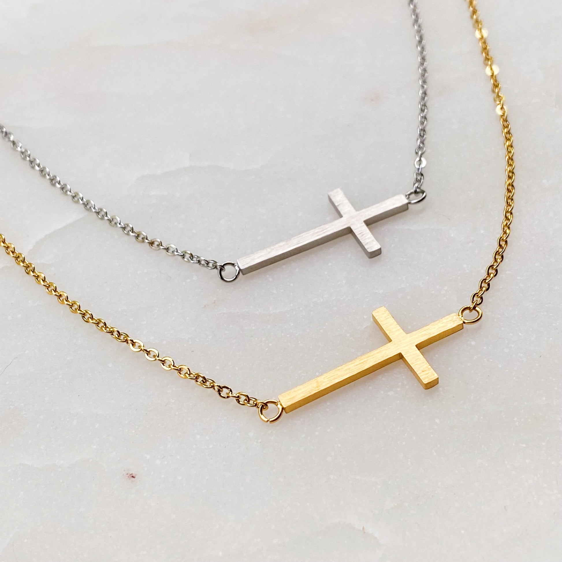 Two cross necklaces, one gold and one silver, on a light background.
