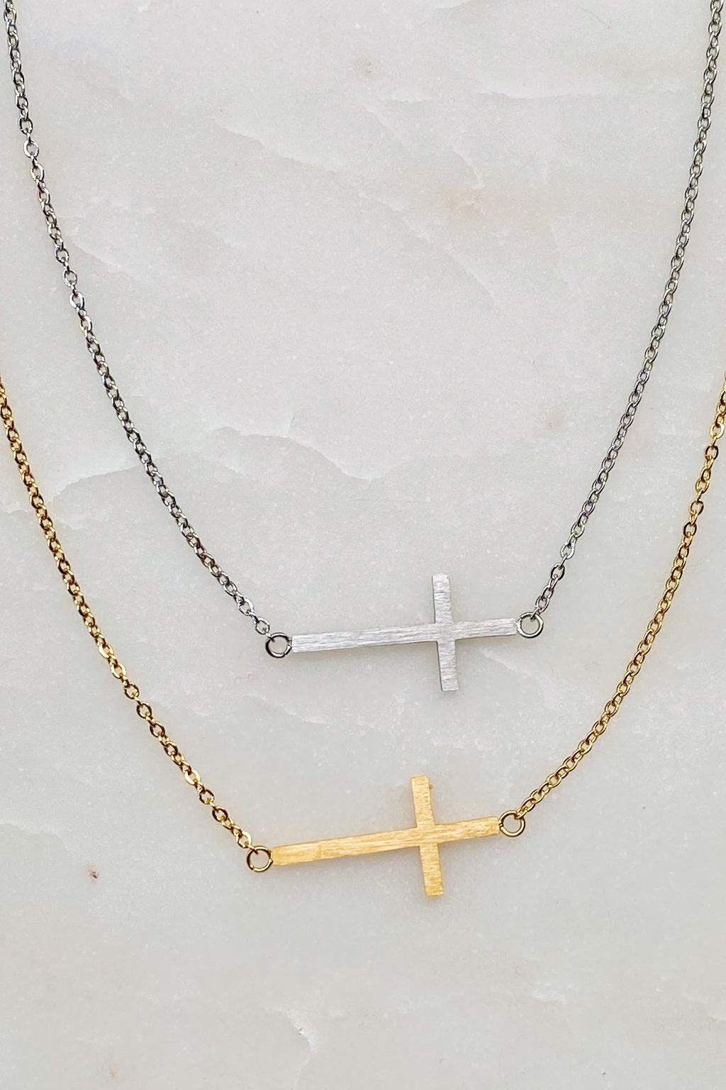 Two cross-shaped necklaces on a marble surface