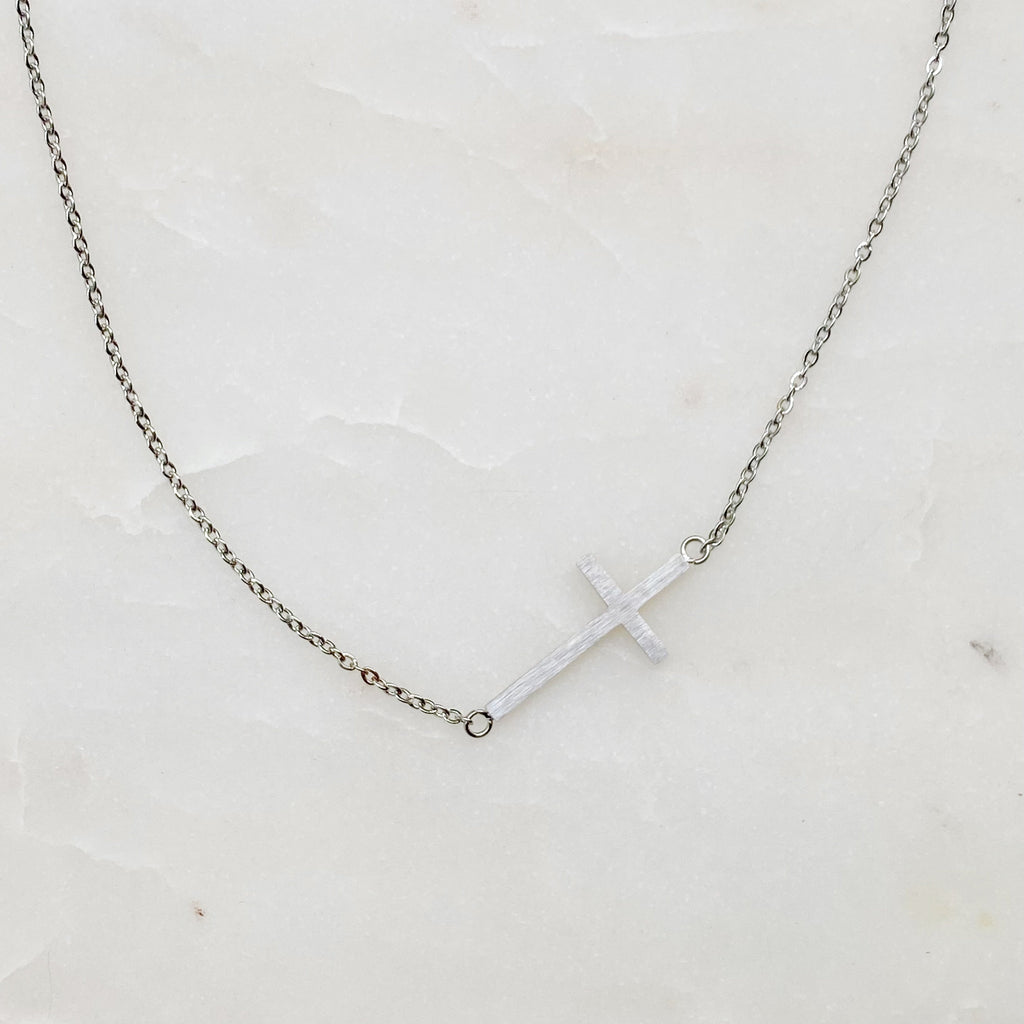 Silver necklace with a cross pendant on a white marble surface