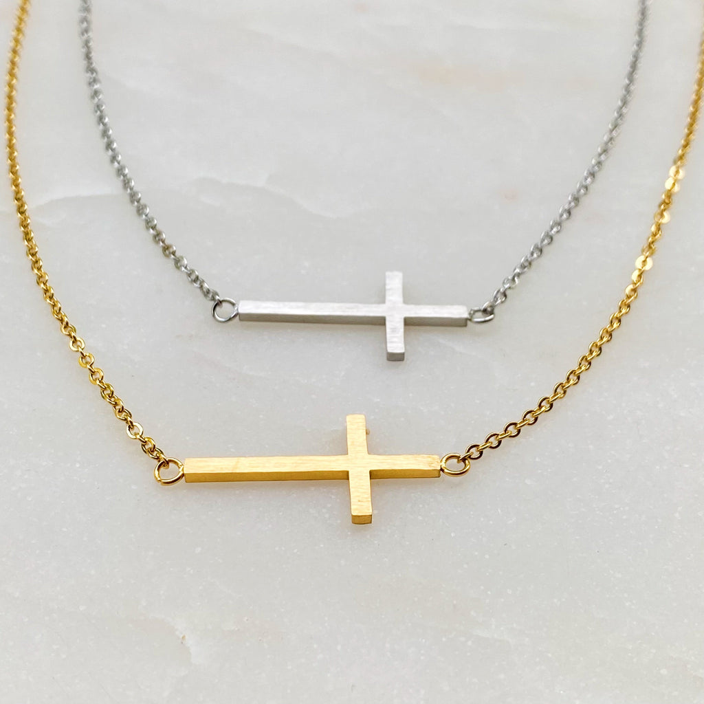 Two cross-shaped necklaces on a light gray surface